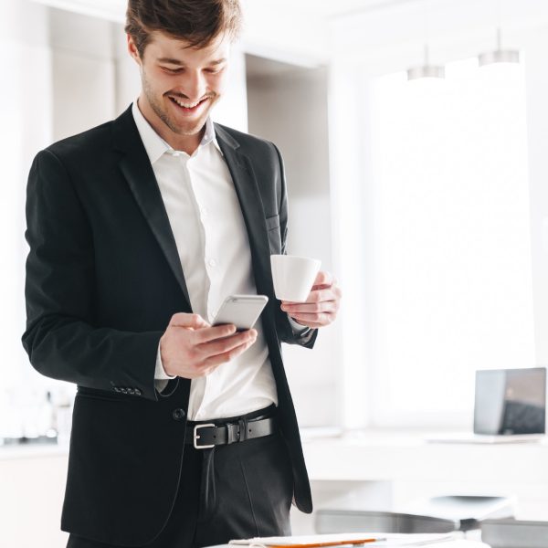 Photo of smiling businessman drinking coffee and using cellphone
